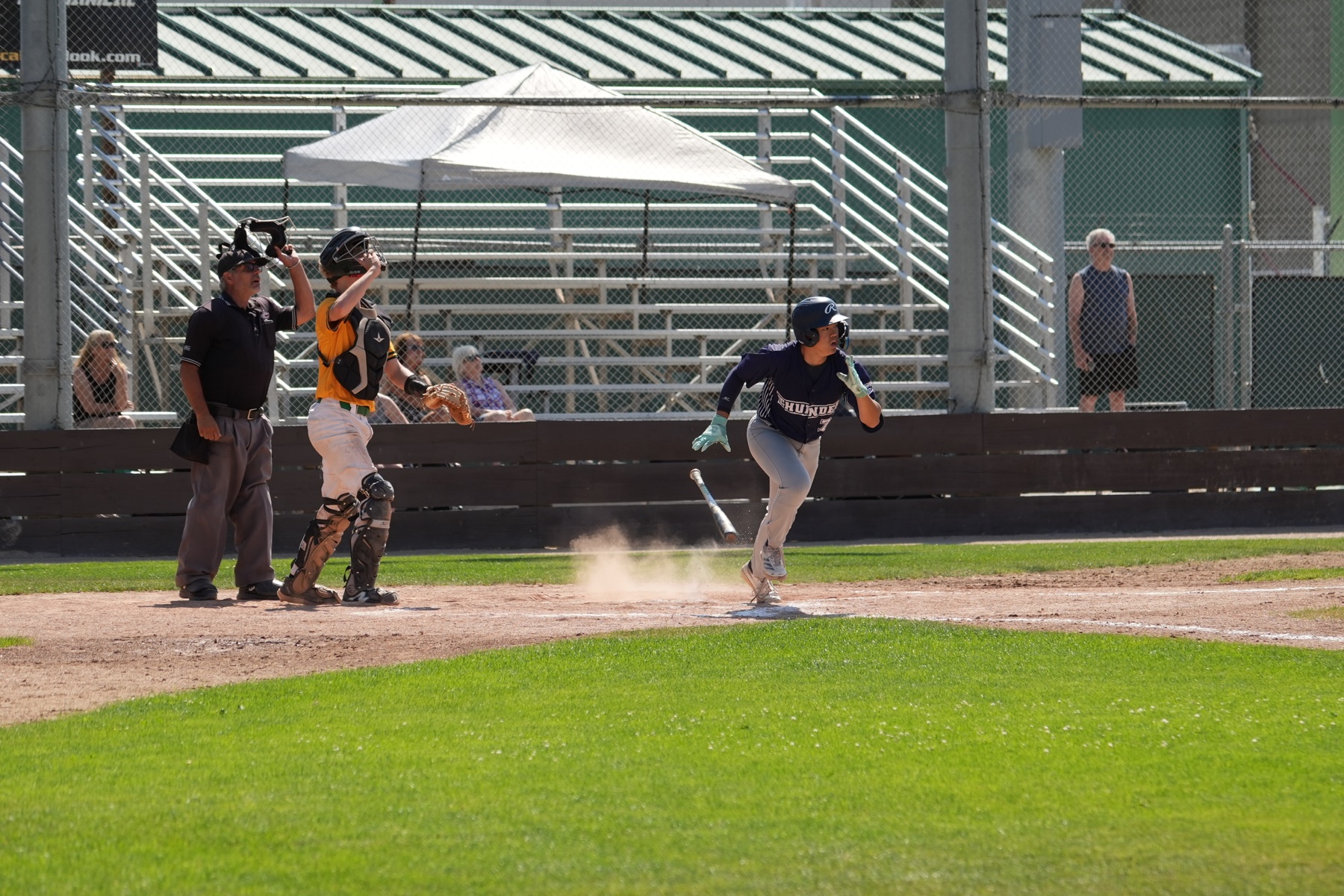 Christopher sprinting out of the batter's box after making contact while a catcher and umpire stand behind home plate.