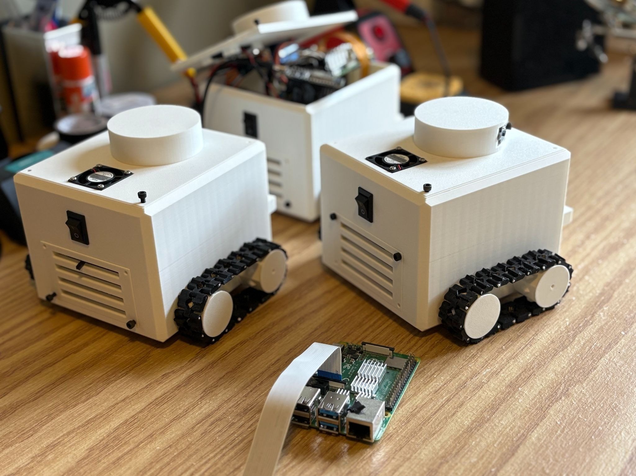 Tracked swarm robot prototypes on a workbench with electronics hardware in front.